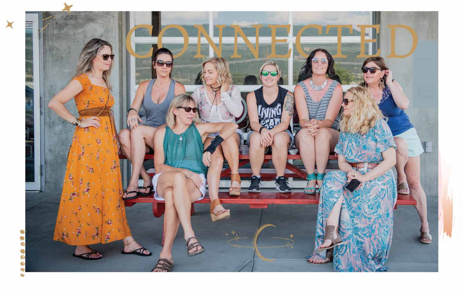 Eight women in boho attire posing for a photo on a red bench with a decorative border and text 'Connected'.