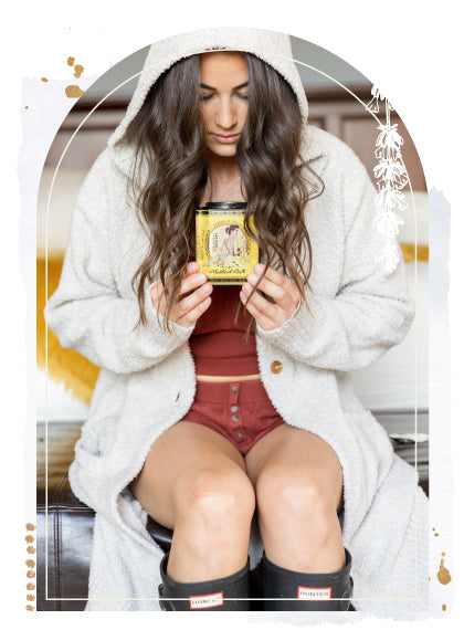 Woman with long brown hair holding Barefoot Venus Mustard bath, bath soak with a decorative frame.