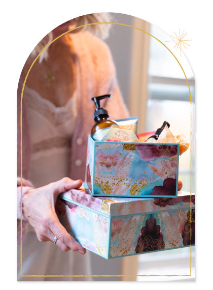 Person holding Barefoot Venus gift boxes with Barefoot Venus products surrounded by a decorative frame.