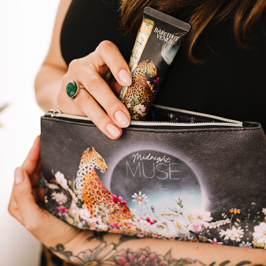 Woman holding pouch with leopard and flower design with text 'Midnight Muse'. A  product is being pulled out of the pouch.