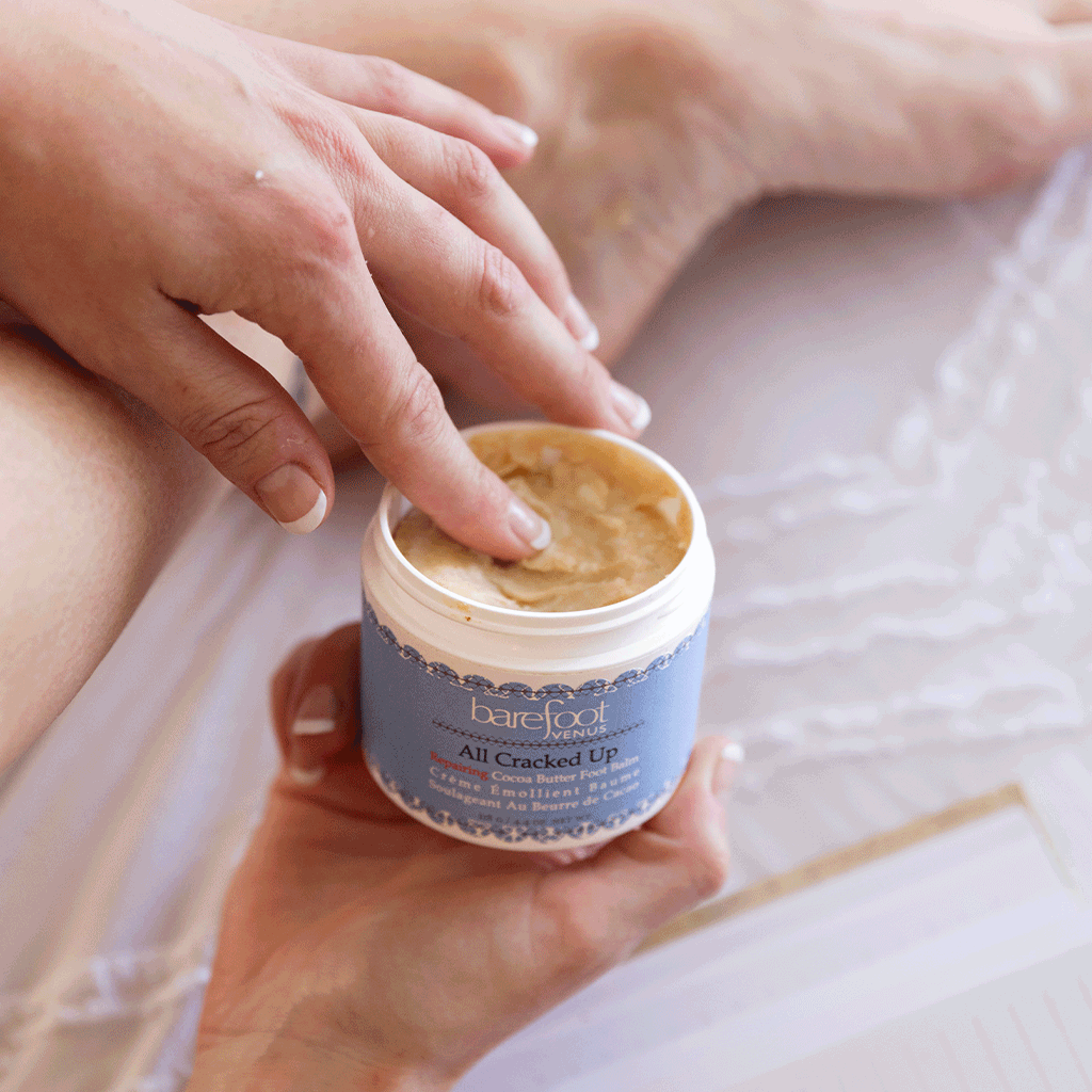 Person using Barefoot Venus All Cracked Up foot balm with blurred background.