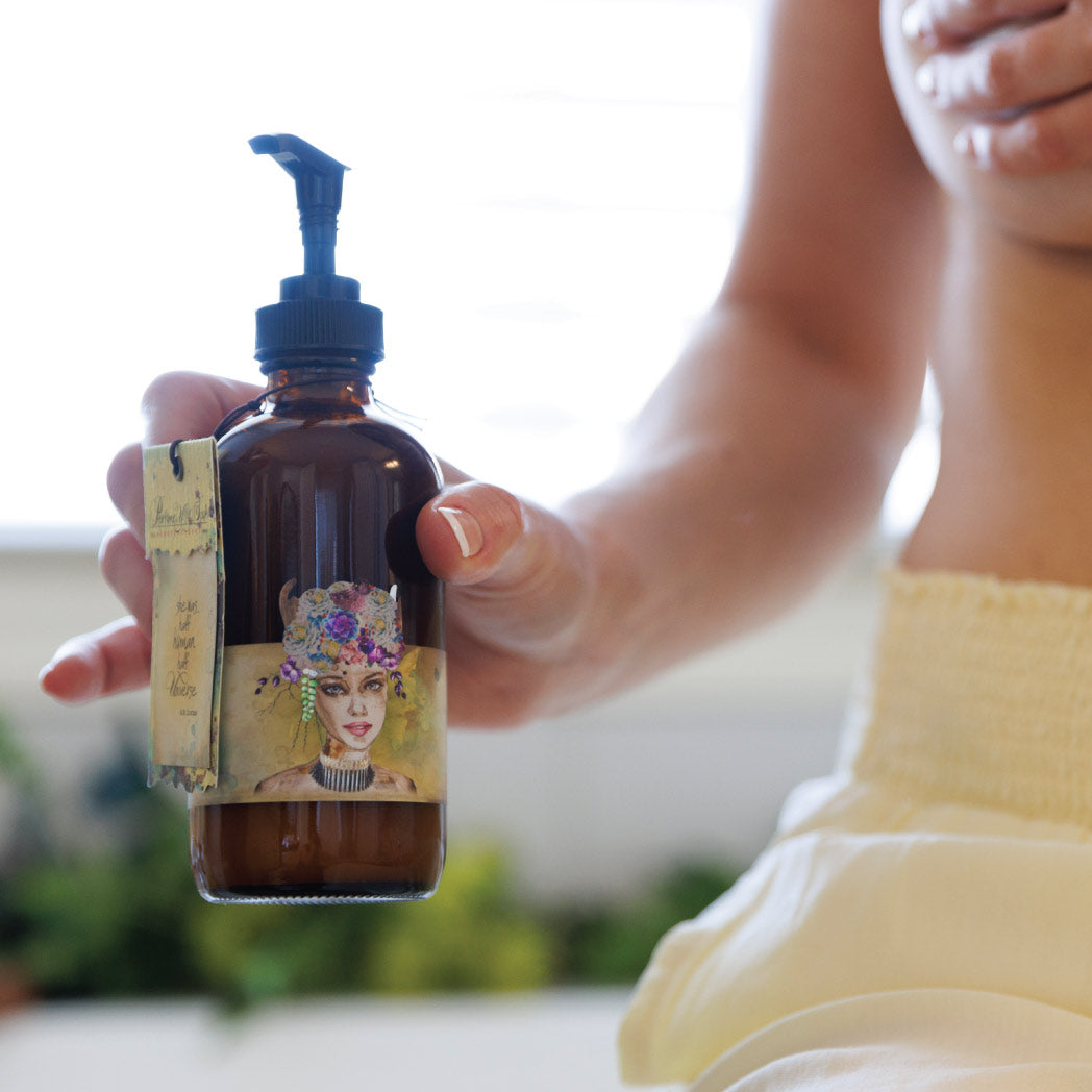 A person holding a bottle of Lemon Freckle body cream with a pump dispenser. The label on the bottle features an illustration of a woman's face with freckles and a floral crown.