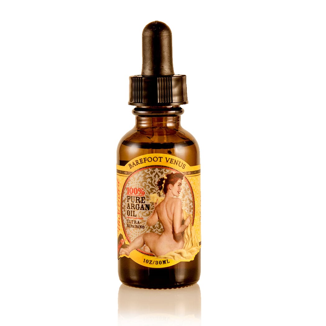 A dropper bottle of Barefoot Venus 100% Pure Argan oil with a vintage design on the packaging with a wooden greenery background.
