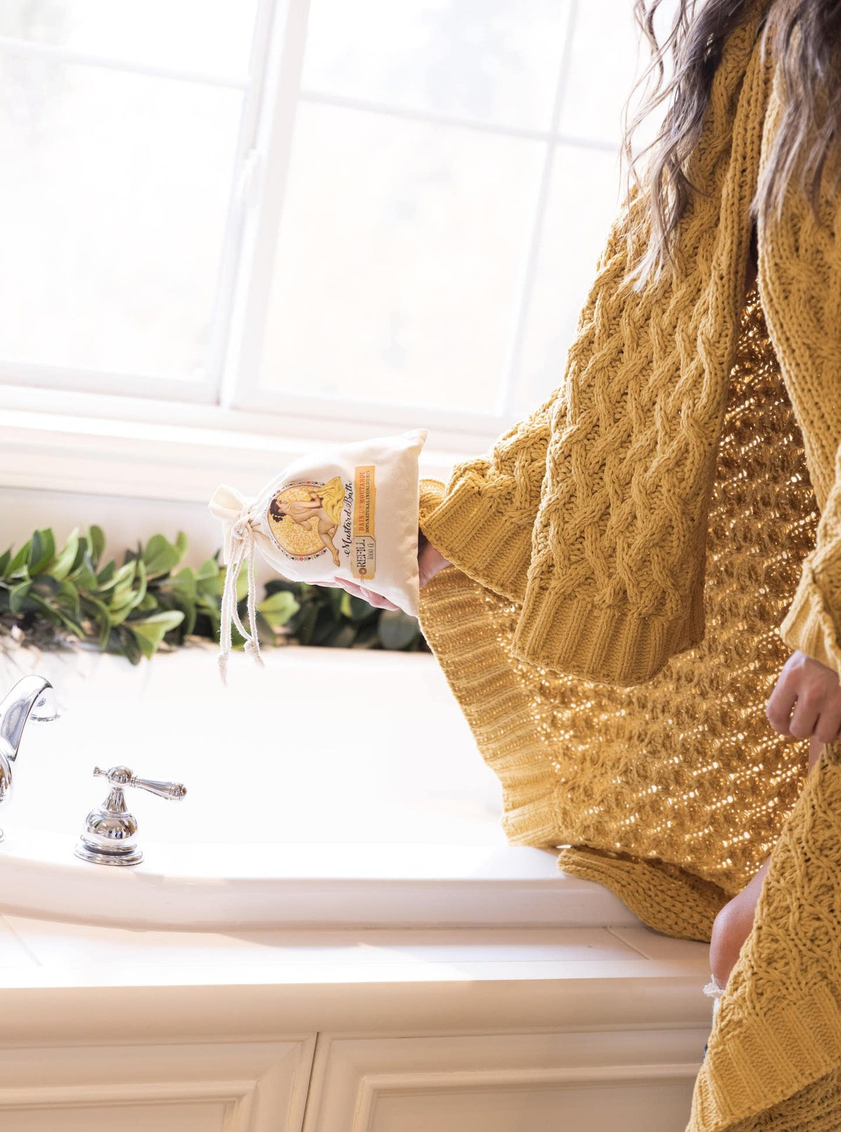 Person wearing a yellow sweater pouring Barefoot Venus mustard bath into a bath tub.