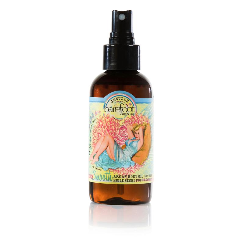 A spray bottle of Barefoot Venus Coconut Kiss Argan body oil with a woman in a blue dress with a floral background design on the packaging on a white background.