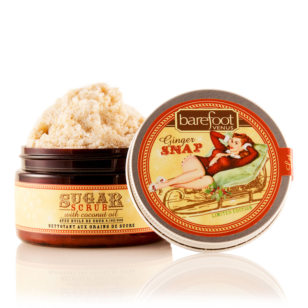 Container of Barefoot Venus Ginger Snap sugar scrub product featuring a woman in a red outfit lying in a toboggan design on a white background.