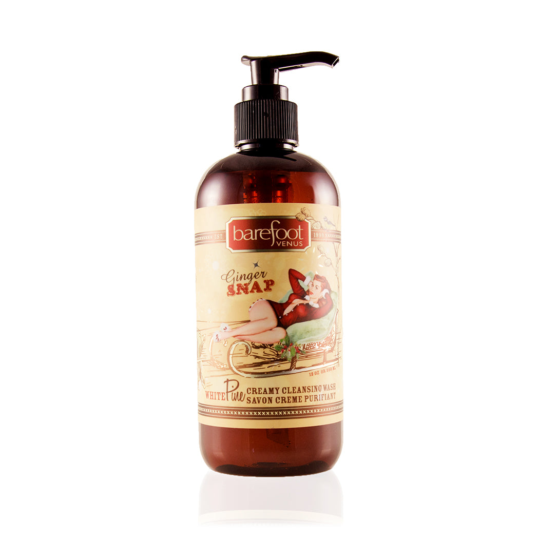A dark brown bottle with a pump dispenser of Barefoot Venus Ginger Snap creamy cleansing wash featuring a woman in a red outfit lying on a toboggan design with a white background.