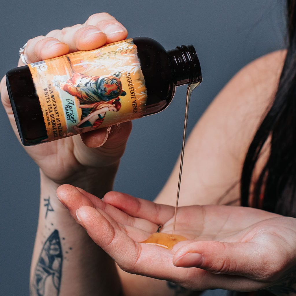 A person pouring a bottle of Apricot Brandy bubble bath onto hand with a label featuring illustrations of tiger and woman.