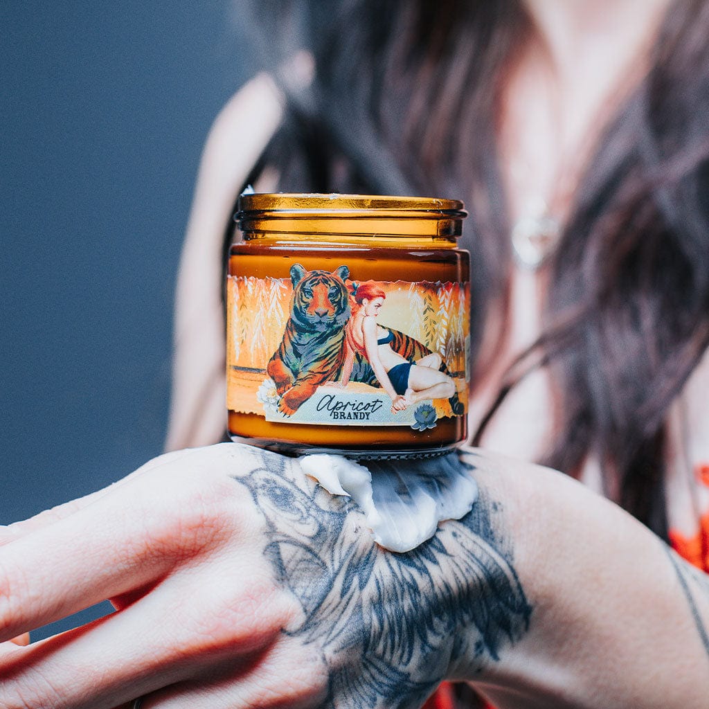 A jar of Apricot Brandy hand repair cream with a label featuring an illustration of a woman and a tiger against an orange and yellow background.