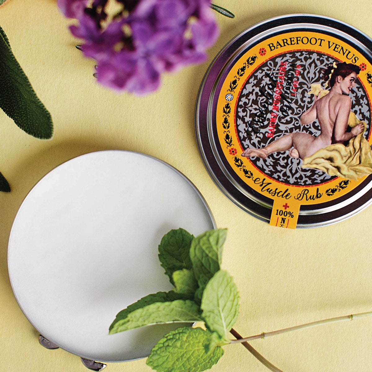 Barefoot Venus Muscle Rub tin with spearmint and flowers on a yellow background.