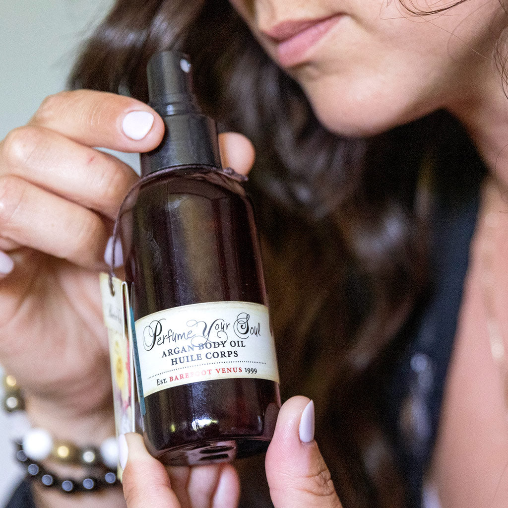 A dark brown bottle with a spray dispenser of Barefoot Venus Black Coconut Argan body oil and a floral zebra design.