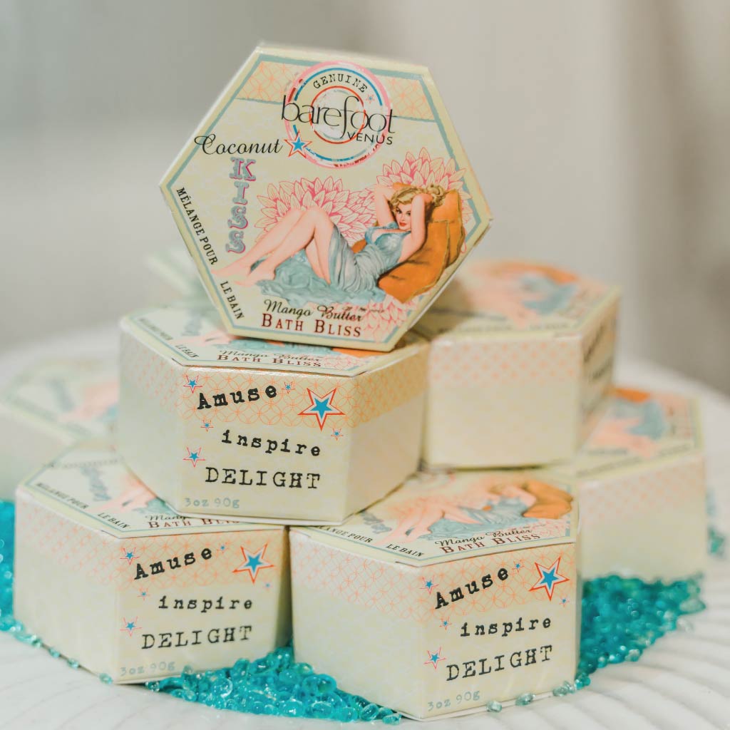 Container of Barefoot Venus Coconut Kiss bath bliss product featuring a woman in a blue dress with a floral background design on a white background.