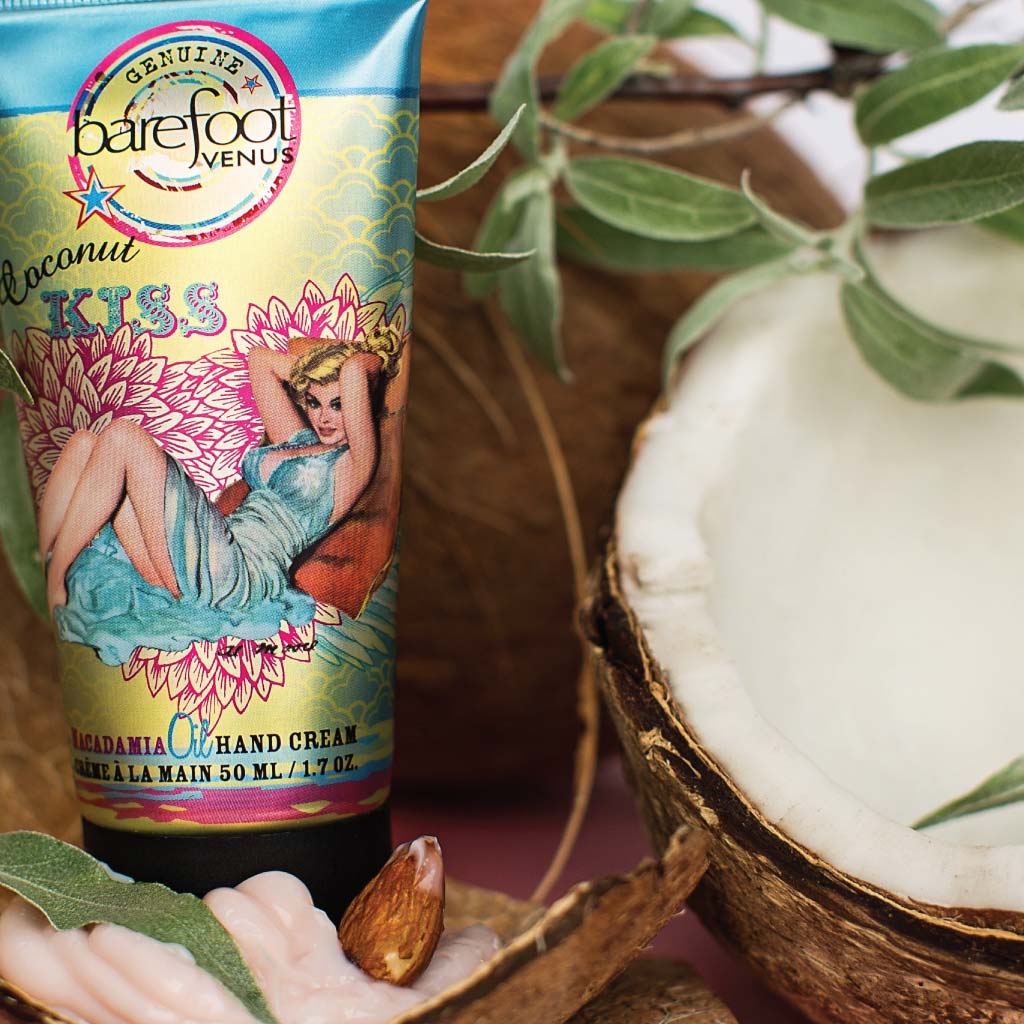 Tube of Barefoot Venus Coconut Kiss hand cream featuring a woman in a blue dress with a floral background design with a blurred background of coconuts and greenery.