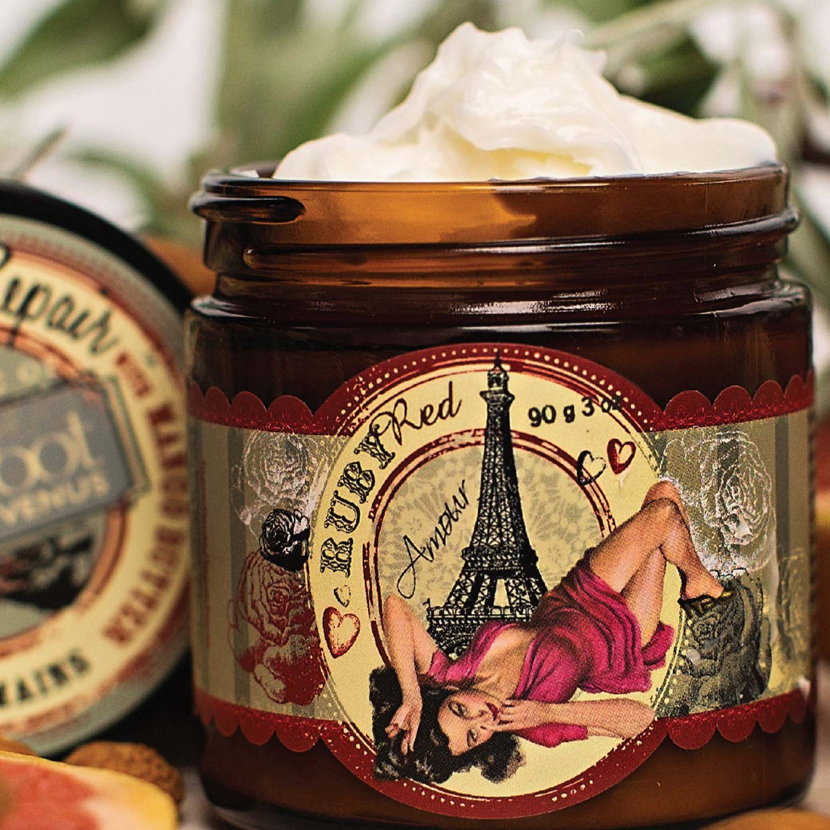 A jar of Barefoot Venus Red Ruby instant hand repair with product overflowing and a woman in a red dress in front of the Eiffel tower design with a blurred background.