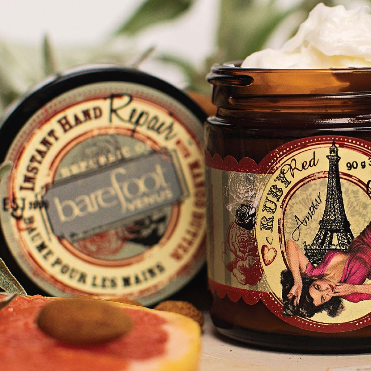A jar of Barefoot Venus Red Ruby instant hand repair with product overflowing and a woman in a red dress in front of the Eiffel tower design with a blurred background of the products lid.