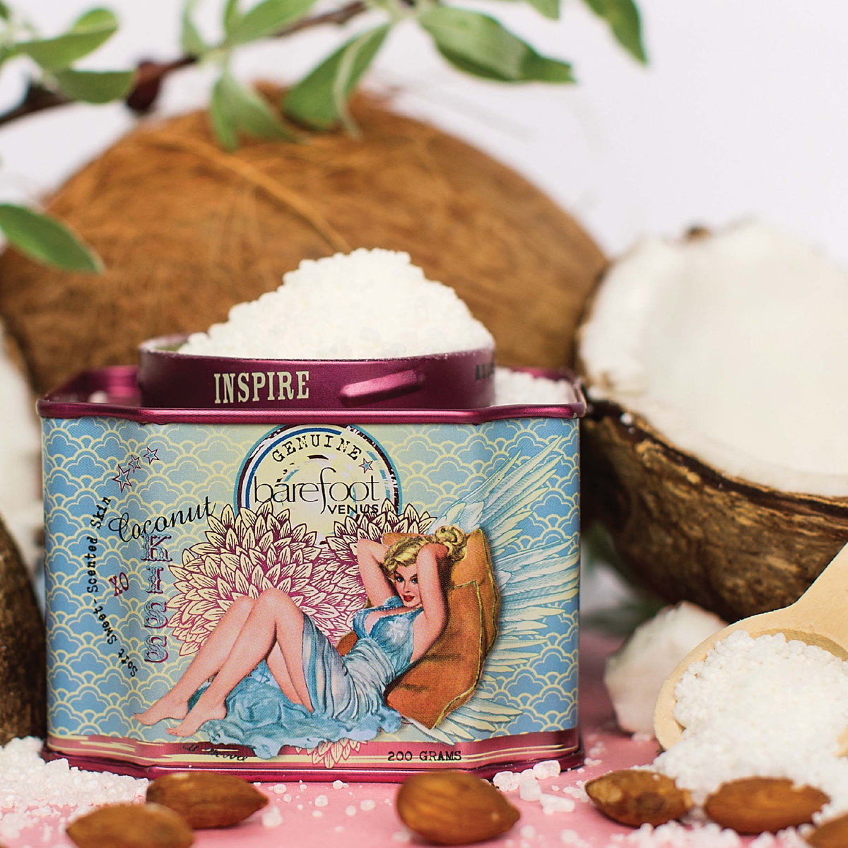 Tin of Barefoot Venus Coconut Kiss bath soak product featuring a woman in a blue dress with a floral background design with coconuts in the background.