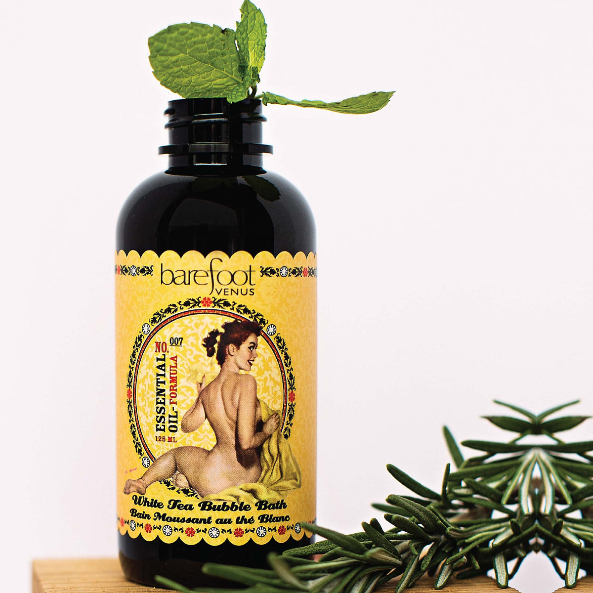 Bottle of Barefoot Venus Essential Oil bubble bath product featuring a vintage design with greenery in the background.