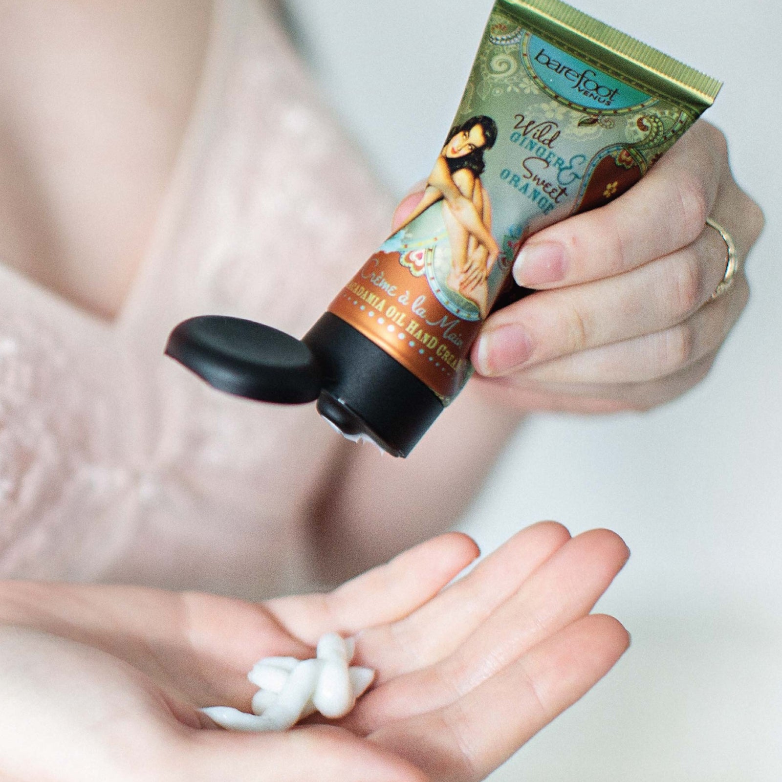 Person dispensing a tube of Barefoot Venus Wild Ginger & Sweet Orange hand cream onto their hand.